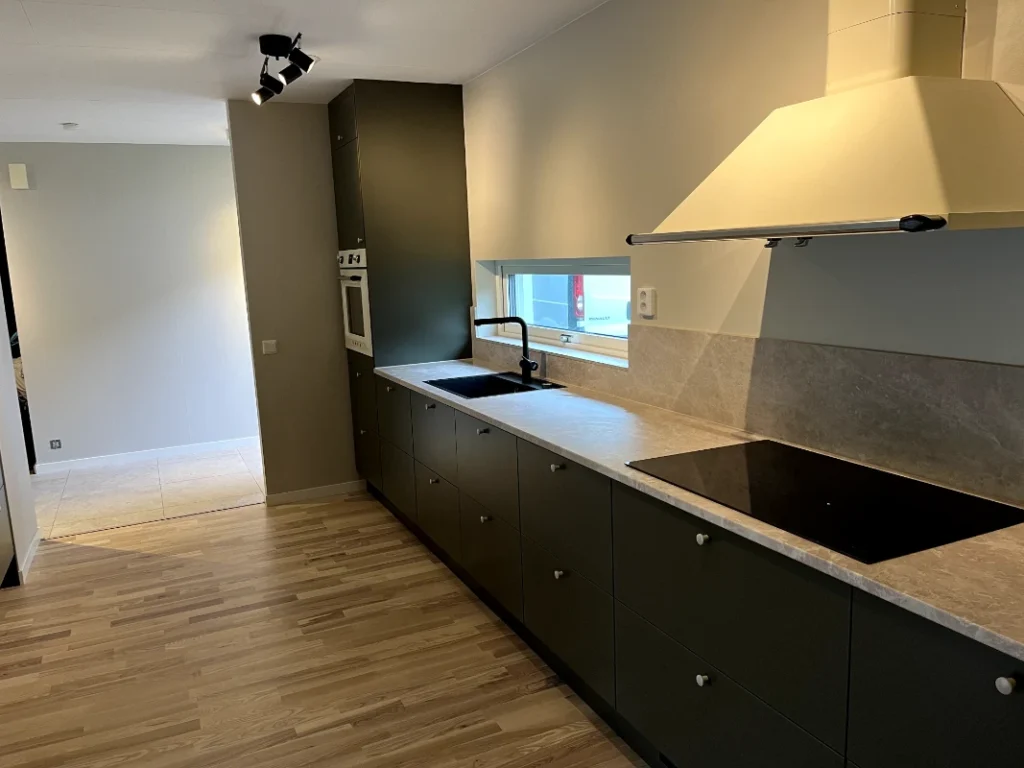 Modernt kök med vita skåp och marmorbänk i Fristad efter renovering, trädetaljer och rostfria vitvaror skapar elegans.